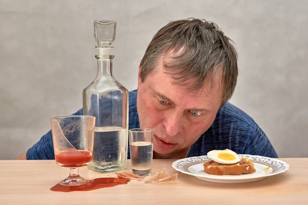 Алкоголик в запойном состоянии за столом с бутылкой