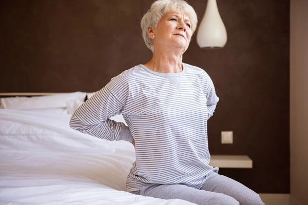 женщина с болью в спине сидит на кровати